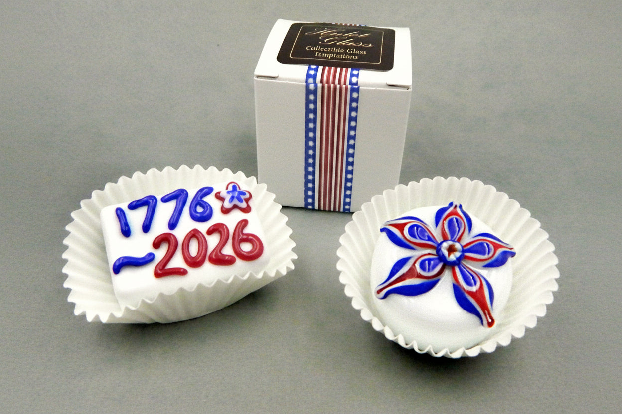 Two decorative glass chocolates with '1776-2026' and star design on a gray background